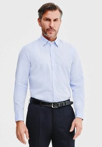Jasnoniebieska koszula z długim rękawem, z klasycznym kołnierzykiem i zapięciem na guziki, w połączeniu z ciemnymi spodniami i czarnym paskiem. Gładka faktura materiału.