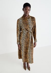 Abito midi a stampa leopardata con maniche lunghe, chiusura frontale con bottoni e cintura da annodare. Il materiale sembra morbido con una texture liscia.