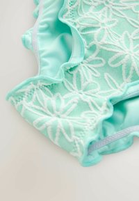 Mentrohelene ujumisriided tekstureeritud lillelisusega tikandi ja volditud servadega, millel on sile sisevooder ja kontrastne õmblus.