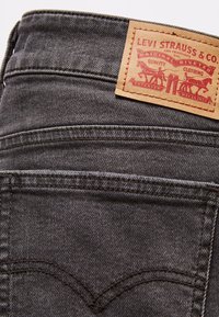 Gros plan sur la poche arrière d'un jean en denim noir avec un écusson en cuir de la marque Levi Strauss & Co. cousu au-dessus de la poche.