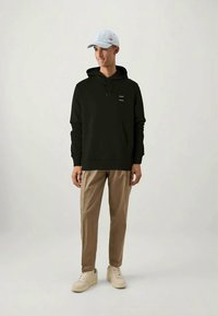 Melnā kapuce ar priekša kabatu un minimālu tekstu, apvienota ar beigu biksēm un baltām sporta apaviem. Cepure ir gaiši zila.