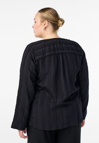 Crna, teksturirana majica s izrezom na leđima, dugim rukavima i horizontalnim prugama na jarmu. Glatka tkanina s opuštenim krojem.