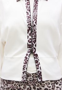 Λευκό μπουφάν με φερμουάρ και λεπτομέρειες με λεοπάρ σχέδιο κατά μήκος του φερμουάρ. Διαθέτει γιακά τύπου mock και εφαρμοστή σχεδίαση, σε συνδυασμό με παντελόνι λεοπάρ.