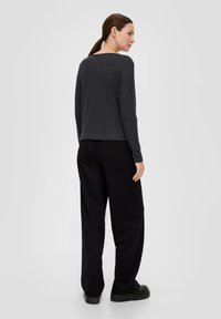 Dunkelgraues Langarmoberteil mit Rundhalsausschnitt, kombiniert mit lockeren schwarzen Hosen und klobigen schwarzen Schuhen. Glatte Stoffstruktur, minimalistisches Design.