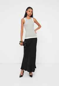 Top cinzento sem mangas e saia maxi preta. O top tem uma bainha branca; a saia cai suavemente, combinada com saltos pretos e uma pequena mala.