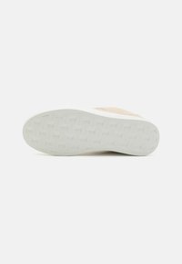 Beige semsket sneaker med en teksturert hvit gummisåle, med et mønstret bunn for grep og minimalistisk design.