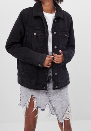 Veste en denim noir avec un col en fausse fourrure texturé. Comprend des poches poitrines à boutons et une coupe décontractée, accompagnée d'une jupe en denim déchirée.