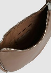 Interiorul unei genți maro din piele, cu un finisaj neted, având un închidere cu fermoar și un mic buzunar interior pentru carduri. Detalii subtile de cusătură.