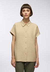 Camicia beige a maniche corte con bottoni, in tessuto testurizzato, colletto a punta e vestibilità dritta. I bottoni sono posizionati lungo la parte anteriore.