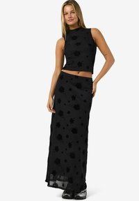 Svart ermeløs crop-top og matchende lang skjørt med blomsterprint, laget av mykt stoff med en litt gjennomsiktig kant.