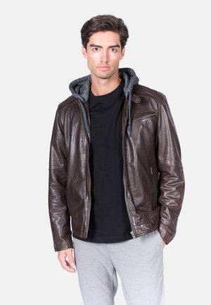 Giubbotto in pelle marrone con cappuccio grigio, chiusura con zip, tasche laterali e finitura testurizzata, indossato sopra una maglietta nera e pantaloni grigio chiaro.