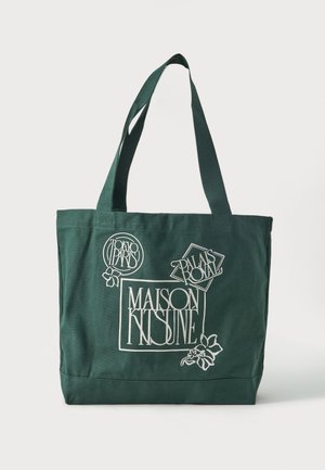 Σκούρα πράσινη τσάντα tote με φαρδιές λαβές, με λευκά γραφικά κείμενα: «Maison Kitsuné», «Tokyo Paris» και «Palais Royal» με ανθικά διακοσμητικά στοιχεία.