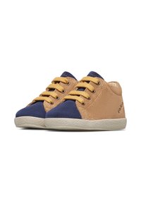Petites chaussures pour enfants avec des côtés en daim beige, des embouts de couleur bleu marine, des lacets jaunes et des semelles blanches texturées sur fond blanc.