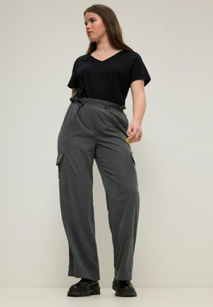 Camiseta negra de cuello en V combinada con pantalones cargo grises de talle alto y corte holgado, con bolsillos laterales y cintura con cordón, usados con botas negras.