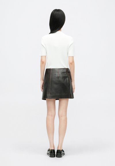 Jupe noire en cuir en forme de A avec des coutures contrastantes, associée à un haut à manches courtes en maille blanche. Texture lisse, coupe décontractée.