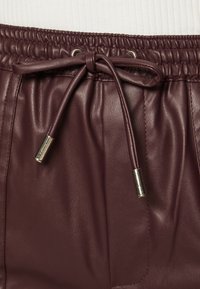 Shorts en cuir bordeaux avec une taille élastique, un cordon de serrage avec des embouts métalliques et une texture lisse.