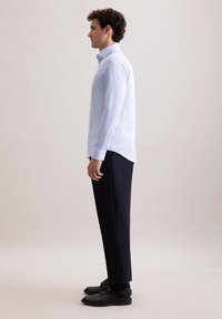 Camicia a maniche lunghe azzurro chiaro con colletto a punta, abbinata a pantaloni e scarpe neri. Tessuto morbido, design aderente e dettagli con bottoni.