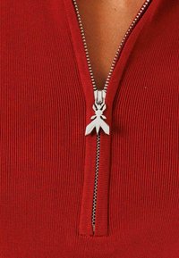 Top in tessuto rigato rosso con una cerniera argento e un originale tirazip a forma di farfalla. Il design è aderente con collo alto.