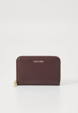 Burgundy leather wallet with a textured finish, gold logo, and zipper closure. Features a small gold hardware accent.