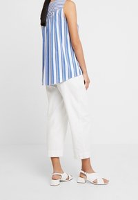 Top senza maniche a righe blu e bianche con retro plissè, abbinato a pantaloni bianchi tagliati e sandali bianchi con tacco a blocco.