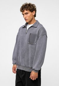 Grijze pullover sweatshirt van zacht materiaal, met een halve ritssluiting, een voorzak en geribde manchetten en zoom. Ontworpen met een relaxte fit.