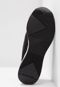 Sneaker nera con suola in gomma testurizzata, caratterizzata da dettagli in mesh neri ben visibili e un accento bianco. Marchio visibile sulla suola.