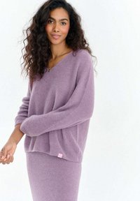 Fioletowy sweter z mieszanki moheru z dekoltem w serek, luźnym krojem i prążkowanym dołem. Posiada długie rękawy oraz małą różową metkę marki po boku.