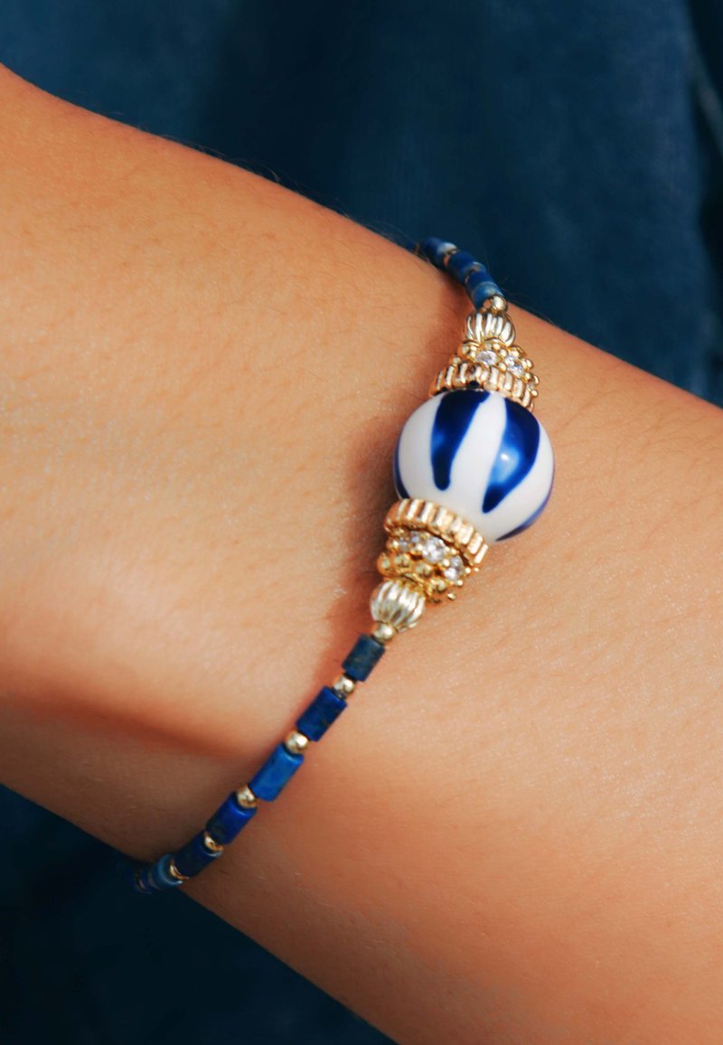 Bracelet en perles bleues et blanches avec une grande perle décorative, des accents dorés et de petites perles rectangulaires et rondes dans une teinte de bleu foncé.