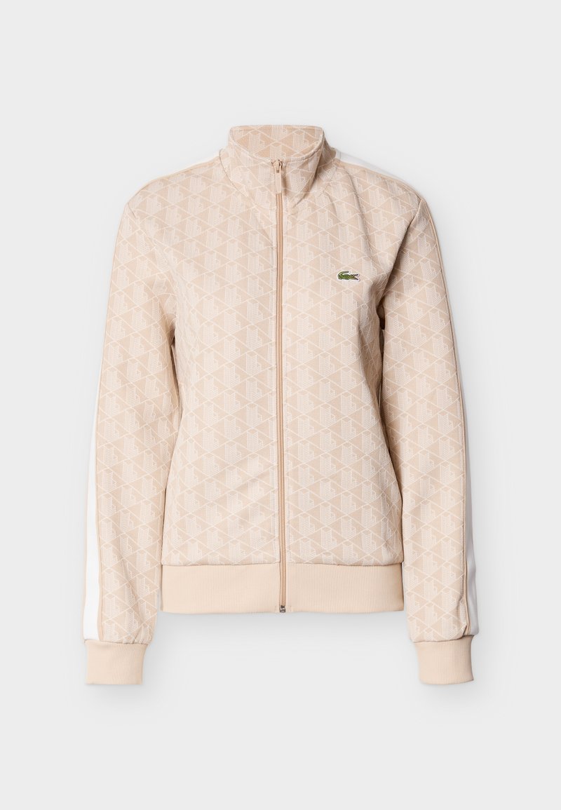Veste beige zippée avec motif géométrique, col haut, poignets et ourlet côtelés, bandes blanches sur les côtés, petit logo crocodile vert sur la poitrine.