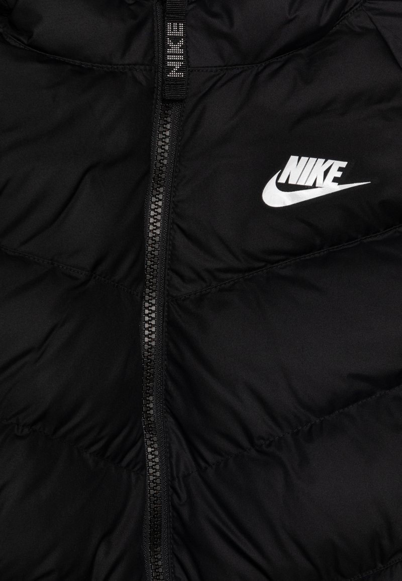 Czarna puchowa kurtka wykonana z gładkiego, pikowanego materiału. Posiada zamek błyskawiczny z przodu oraz wyraźne białe logo Nike na klatce piersiowej.