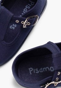 Námořnické plátěné boty s kulatou špičkou, přezkou a nazouvacím designem. Uvnitř je vidět název značky "Pisamonas" v světle modré barvě.