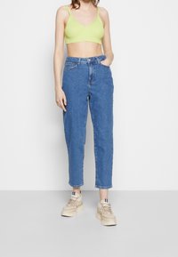 Světle zelený žebrovaný crop top, modré džíny s vysokým pasem a béžové tenisky. Hladká textura, design rovného nohavice a minimální detaily.