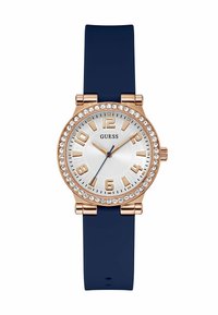 Guessi kell, millel on roosaka kuldse äärise ja kristalle täis detailid, hõbedane kellasi, sinine silikoonist rihm ja julged araabia numbrid.