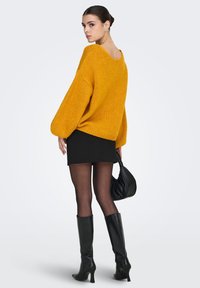 Strikket oransje genser med oversized ermer, svart miniskjørt, gjennomsiktige strømpebukser og svarte støvler med hæl som går til knærne, kombinert med en svart håndveske.