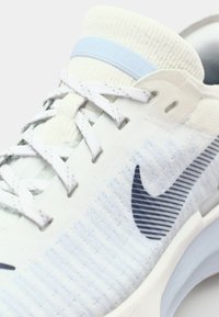 Light blue and white Nike running shoe featuring a textured knit upper, white laces, and a navy logo. Outsole has a soft, cushioned look.