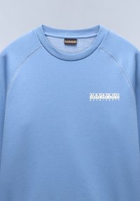 Felpa azzurra chiara realizzata in un tessuto liscio, con un colletto rotondo a coste e un logo bianco sul lato sinistro del petto. Maniche raglan flessibili.