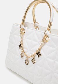 Biała pikowana skórzana torebka z złotymi okuciami, dwoma zaokrąglonymi uchwytami i ozdobnym złotym łańcuszkiem z czarnymi i złotymi akcentami.