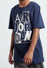 Námořnická bavlněná tričko s velkým b�ílým a vzorovaným grafickým prvkem "AIR JORDAN", krátkými rukávy a kulatým výstřihem.