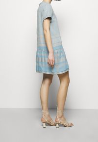 Světle modré šaty s krátkým rukávem a texturovaným vzorem, se volánkovým lemem. V kombinaci s béžovými sandály na podpatku s blokovým podpatkem.