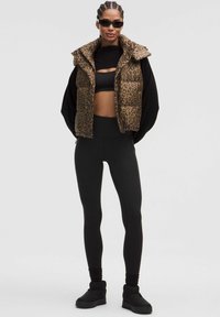 Brun leopardprint puffer vest over en sort crop top, parret med sorte højtaljede leggings og ankelstøvler. Glatte teksturer, tætsiddende stil.