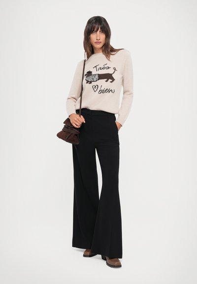 Beige knitted sweater with a dog illustration and text, paired with black wide-leg trousers and brown heeled boots, carrying a brown bag.