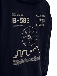 Sort stof med hvidt trykt tekst og grafik, herunder "B-583", "All Terrain Wear", et cirkulært kort mærket "Off Duty Gear" og bygningernes skyline-skitser.