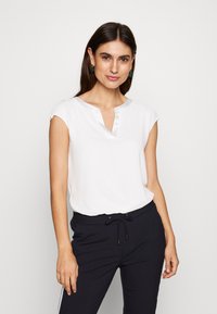 Blouse blanche à manches courtes avec un col en V et un bord de cou en satin, associée à un pantalon bleu marine avec cordon de serrage et bandes latérales.