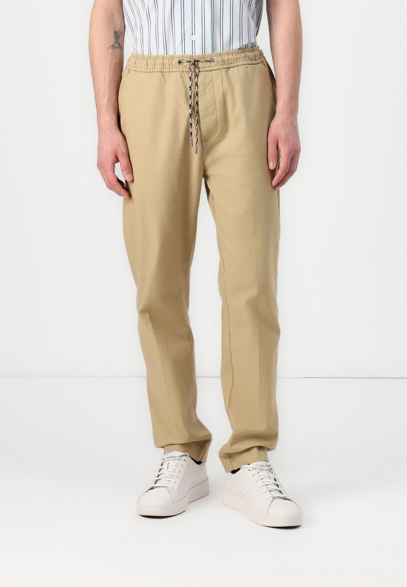 Beige Joggingshosen aus Baumwolle mit elastischem Bund und Kordelzug, versehen mit Seitentaschen und einer lockeren Passform.