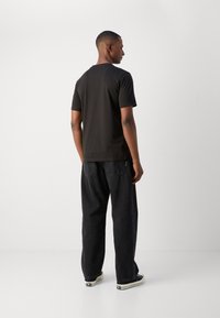 Sort kortærmet t-shirt med tætsiddende design, parret med løse mørke jeans, der har et tekstureret stof, og kontrasterende lysfarvede sko.