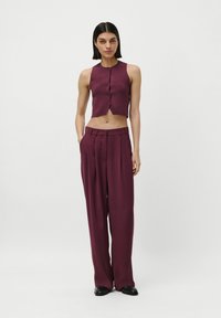 Fialový skrátený bezrukávový top s prednými gombíkmi, v kombinácii s nohavicami s vysokým pásom vo voľnom strihu v zodpovedajúcej farbe. Hladká textúra.