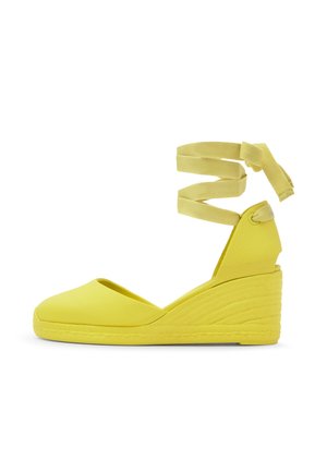 Gele espadrille schoen met een gesloten neus, een gestructureerde hak en lange stoffen enkelbanden die om de enkel gewikkeld zijn.