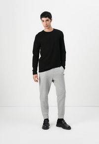 Svart langermet skjorte med rund hals, kombinert med lysegrå smale joggebukser og svarte sko. Glatt stoff, enkel design.