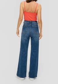 Débardeur rouge ajusté avec des bretelles fines, associé à un jean en denim bleu taille haute et à jambe large, doté de poches arrière et d'une coupe décontractée.