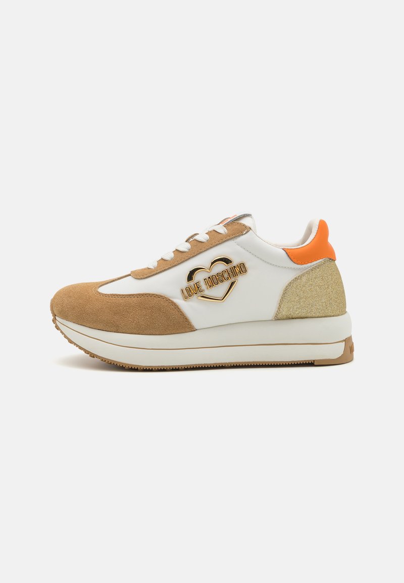 White leather sneakers with tan suede accents, orange heel tab, gold logo, platform sole, and textured detailing on the heel.